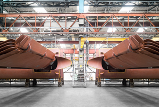 Industriehalle mit zwei riesigen, rostfarbenen Metallkonstruktionen im Vordergrund. Im Hintergrund sind Stahlträger und eine gelbe Krananlage sichtbar.