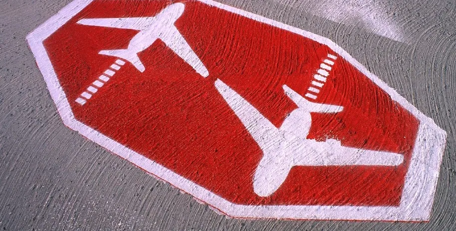 Rote Bodenmarkierung in Form eines Achtecks mit zwei weißen Flugzeug-Symbolen auf grauem Asphalt.