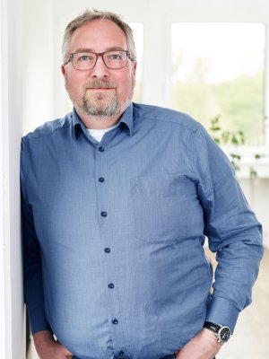 Porträt von Stephan Klein, Head of Customs & Export Service, lächelnd in einem blauen Hemd vor einem hellen Hintergrund.