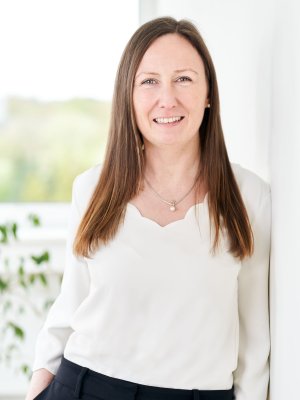 Porträt von Tanja Staufenbiel, Sales Assistant, freundlich lächelnd vor hellem Hintergrund mit Fenster und Pflanze.